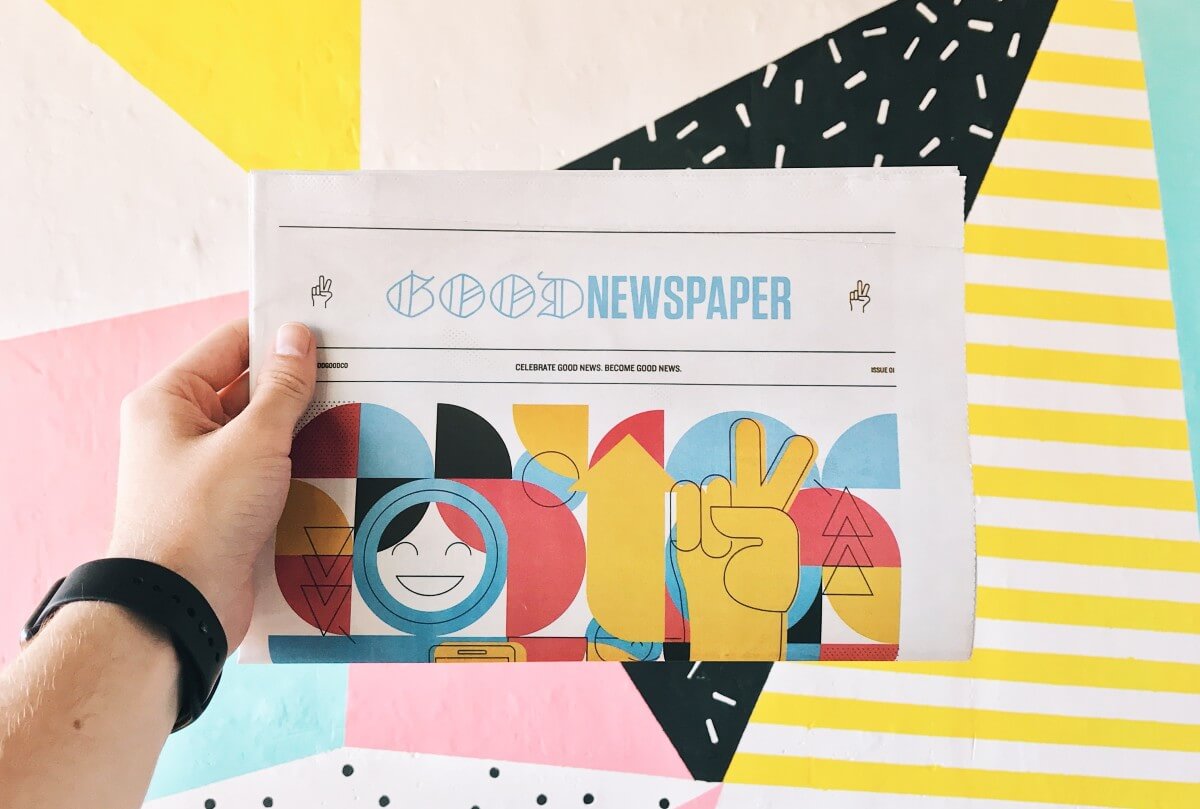Person's arm holding the Good News newspaper on colourful geometric background